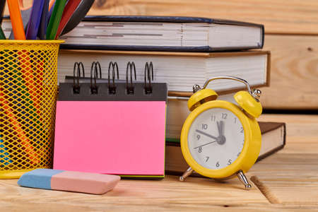 Back to school concept with school supplies. Office desk with alarm clock, blank notebook, pile of books and colorful pencils. Concept of education.の写真素材