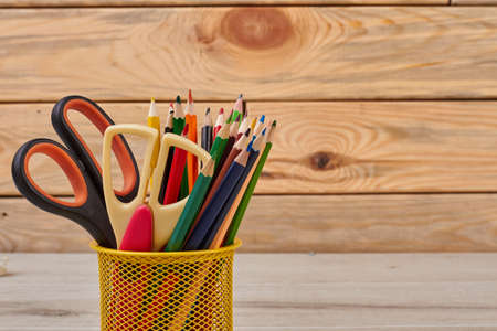 Colored pencils and scissors in basket. Wood color pencils in yellow metal pencil holder. Stationery items and drawing tools.の写真素材