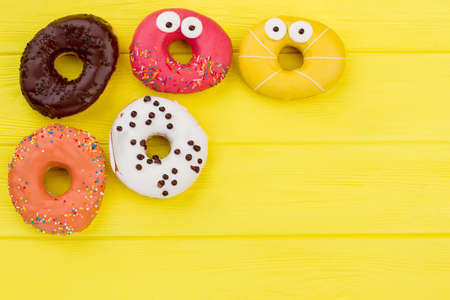 Donuts on yellow background with copy space. Side border of assorted donuts with pastel colored icing and sprinkles.の写真素材