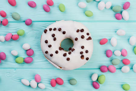 White glazed donut and colorful candies. Sweets on blue wooden background. Holiday party...