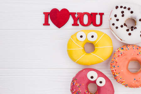 Composition with funny donuts on white wooden table. Colorful donuts and inscription I love you on...