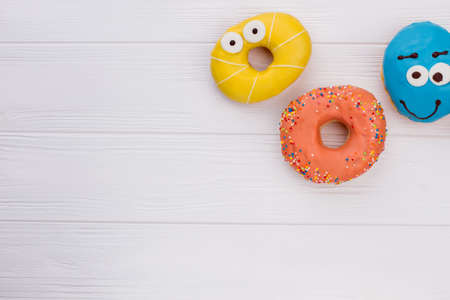 Donuts with funny eyes on wooden background. Iced pastry on wooden surface and copy space. Treats for kids party.の写真素材