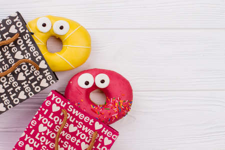 Shopping bags and donuts on wooden background. Paper gift bags and iced donuts with funny face expression. Space for text.の写真素材