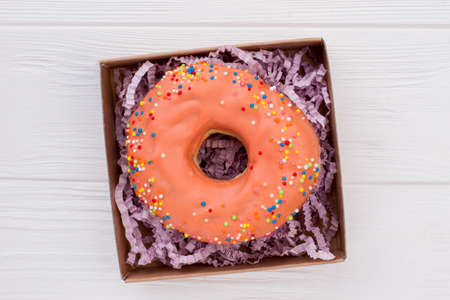 Donut in box on white wooden background. Box with orange cake on wooden table.の写真素材