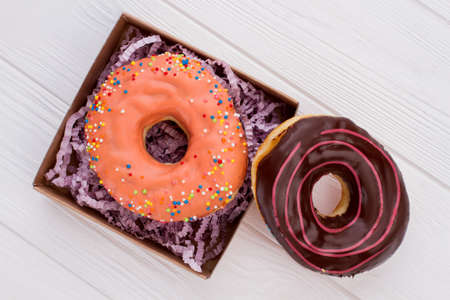 Two different donuts on white wooden background. Frosted cakes on wooden table. Sweets for party.