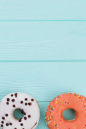 Two different donuts on blue wooden background. Pastry decorated with colorful icing. Holiday of taste.の写真素材