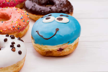 Blue funny donut on wooden table. Glazed decorated donuts for sweet break on white wooden background. Flat lay, copy space.の写真素材