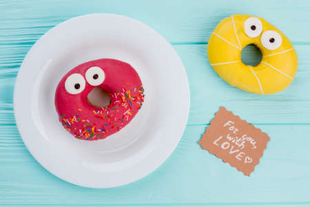 Composition with funny donuts on wooden background. Two surprised doughnuts and card with...