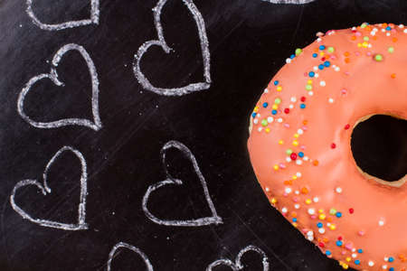 Frosted donut and hand drawn hearts. Orange donut with colorful sprinkles and chalk drawn hearts on black background.の写真素材