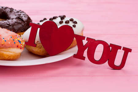 I love you inscription and donuts. Plate with iced donuts on pink wooden background. Love and...