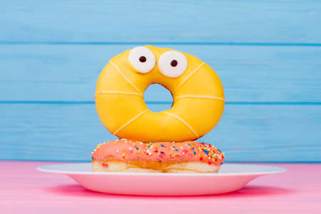 Plate with surprised yellow donut on blue background. Funny donut with shocked face on color...
