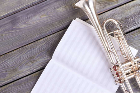 Old trumpet on musical notes sheet. Musical notes and vintage trumpet on wooden background with copy space.の写真素材
