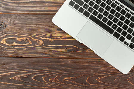 Silver laptop and copy space. Part of laptop computer on brown wooden background with text space. Business and work space concept.の写真素材