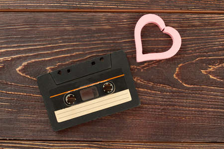 Old analogue cassette and pink heart. Tape cassette and heart-shaped decoration on brown wooden background. Old musical technology and love concept.の写真素材