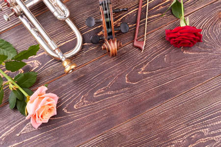 Musical instruments, flowers and copy space. Trumpet, violin and roses on wooden background with text space. Romantic music background.の写真素材