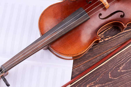 Violin and musical notes close up. Brown vintage violin and bow on wooden background. Symbol of orchestra music.の写真素材