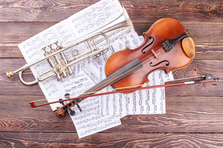 Trumpet and violin on wooden background. Musical notes, volin, bow and trumpet, top view. Classical instruments of orchestra.の写真素材