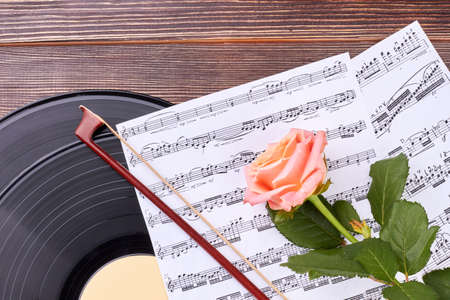 Vintage musical objects and pink rose. Vinyl record, violin bow, musical notes and rose on wooden...