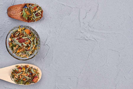 Herbal tea in spoons and bowls. Dry mountain herbal tea on gray background with copy space, horizontal image. Ingredients for healthy natural drink.の写真素材