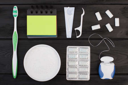 Dental cleaning tools on black background. Toothbrush, dental floss toothpick, chewing gums and blank paper notebook.の写真素材