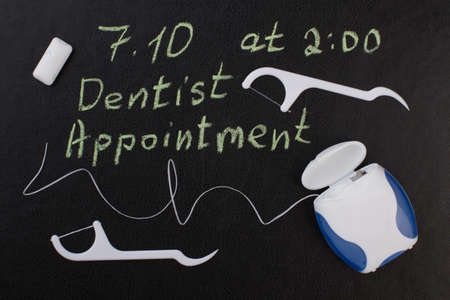 Note dentist appointment and dental floss. Reminder dentist appointment on chalkboard and dental care products.の写真素材