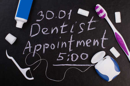Dental care accessories and dentist appointment inscription. Dentist appointment reminder and oral hygiene products on chalkboard.の写真素材