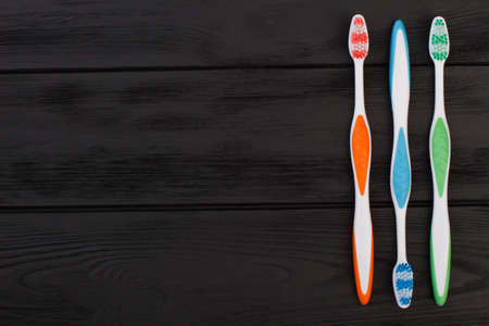 Colorful toothbrushes on black wooden background. Three different tooth brushes on dark surface. Space for text.の写真素材