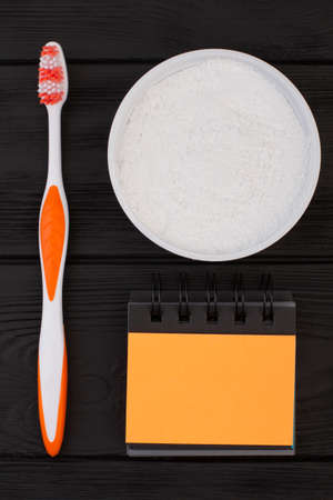 Dental care products on black background. Tooth care with toothbrush, powder for teeth cleaning and blank paper notepad.の写真素材