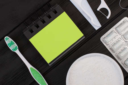 Dental care objects on black background. Toothbrush, blank notebook, powder for cleaning teeth and chewing gums. Dental oral hygiene.の写真素材