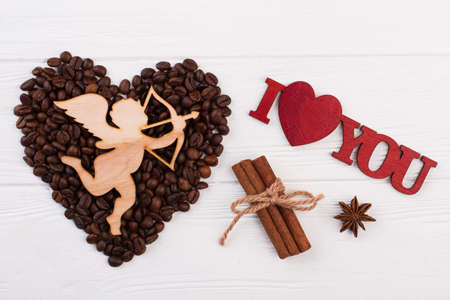 Romantic composition with coffee beans. Heart from coffee beans, wooden cupid with arrow and...