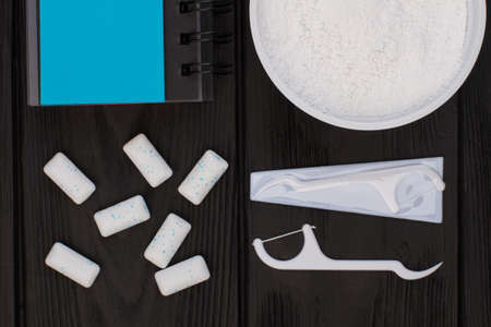 Dental hygiene tools on black background. Powder for teeth cleaning, dental floss toothpick, chewing gums and spiral notepad.の写真素材