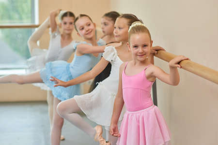 Happy smiling ballerina in pink suit. Adorable little ballet girl standing at ballet barre in studio and looking at camera.の写真素材
