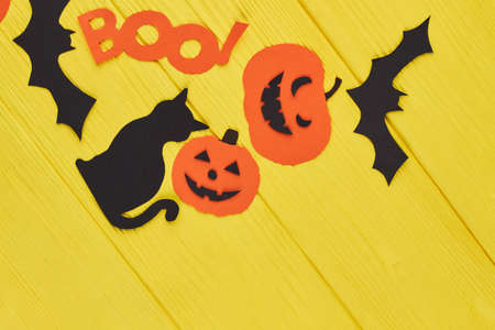 Holiday decorations for Halloween. Cat, bat, pumpkin and word boo cut out of paper on yellow...