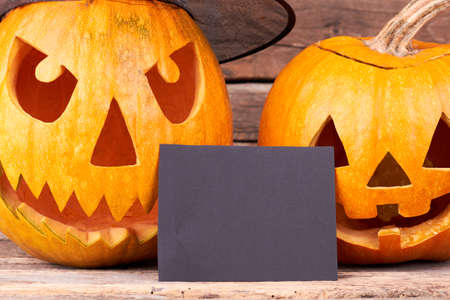 Halloween pumpkins and blank paper card. Close up carved pumpkins for Halloween holiday with blank card for greeting.の写真素材