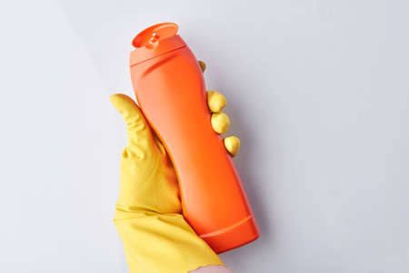 Hand in glove holding orange bottle detergent. Space for text. Spring cleaning background.の写真素材