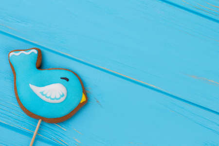 Blue bird shaped biscuit. Cookie on stick on blue wooden background with copy space. Baked Easter treat.の写真素材
