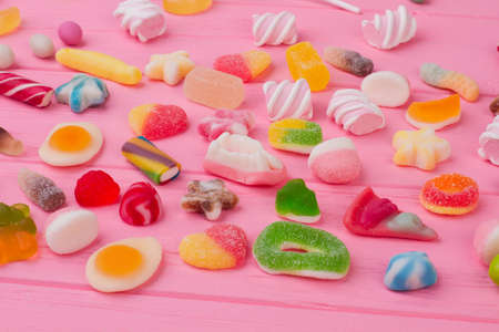 Gummy candies background. Assortment of different jelly candies on pink wood. Delicious treats for kids.の写真素材