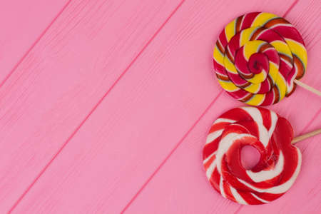 Colorful lollipops on pink wood. Sweet round candies on color woden background with copy space. Holiday invitation card.の写真素材