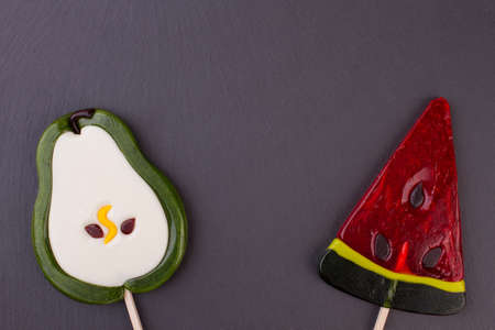 Large lollipops in a shape of fruits. Candies in a form of pear and watermelon on dark background...