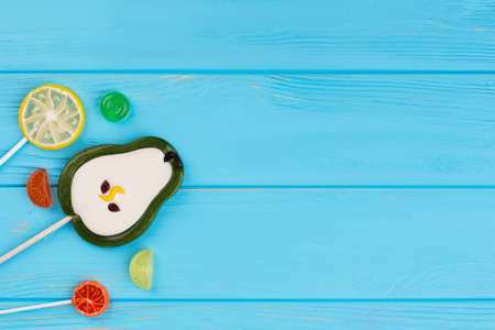 Colorful lollipops in a shape of fruits on blue background. Delicious candies on sticks in a shape...