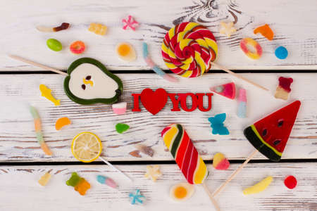 I love you inscription and mixed candies. Romantic background with assorted candies on white wooden background. Valentines Day concept.の写真素材