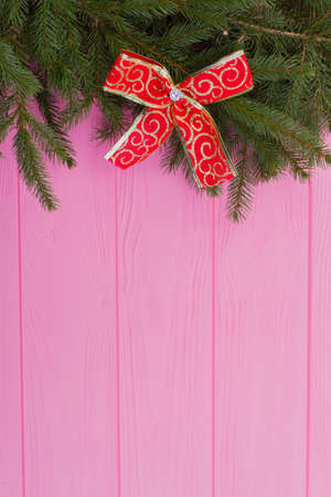 Christmas or New Year background. Fresh fir branches with red bow on pink wooden boards and space for text, vertical image. Natural coniferous decor.の写真素材