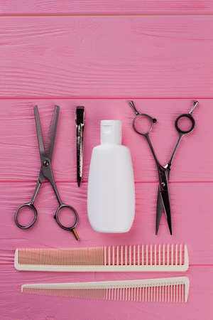 Professional hairdresser tools on pink background. Combs, scissors and shampoo bottle. Beauty salon concept.