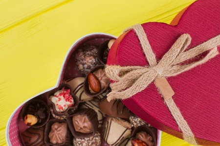 Red heart shaped gift box with chocolate candies. Assorted Chocolates on yellow wooden background. Valentines Day gift.の写真素材