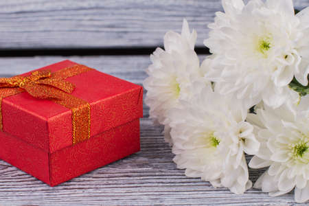 White chrysanthemums and red gift box. Jewelry present box and bunch of fresh flowers. Romantic gift...