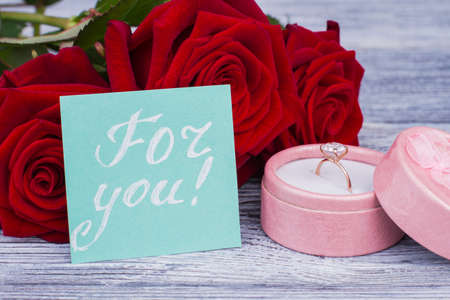 Engagement ring in box and red roses. Beautiful gift box with diamond ring, blooming flowers and...