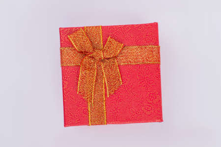Red gift box with golden floral pattern and bow. Elegant red jewelry box with golden bow over gray...