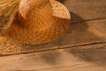 Straw hat and wheat ears on rustic wooden boards. Farmers hat and cereal grain on old wooden floor.の写真素材