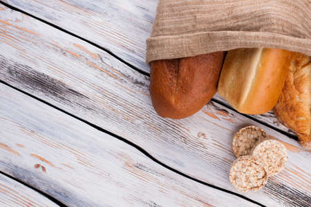 Different kinds of bread in burlap bag on wooden table. Healthy farmers bread. Space for text.