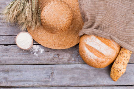 Peasant hat, artisan bread and wheat ears. Rustic still life with bread, wheat ears, hat and bowl with flour.の写真素材